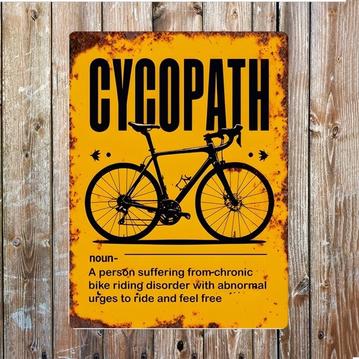 Yellow vintage style sign, showing signs of rust that has a picture of a push bike with the title 'CYCOPATH'. The dictionary style desciption says - 'noun - A person suffering from chronic bike riding disorder with abnormal urges to ride and feel free'.