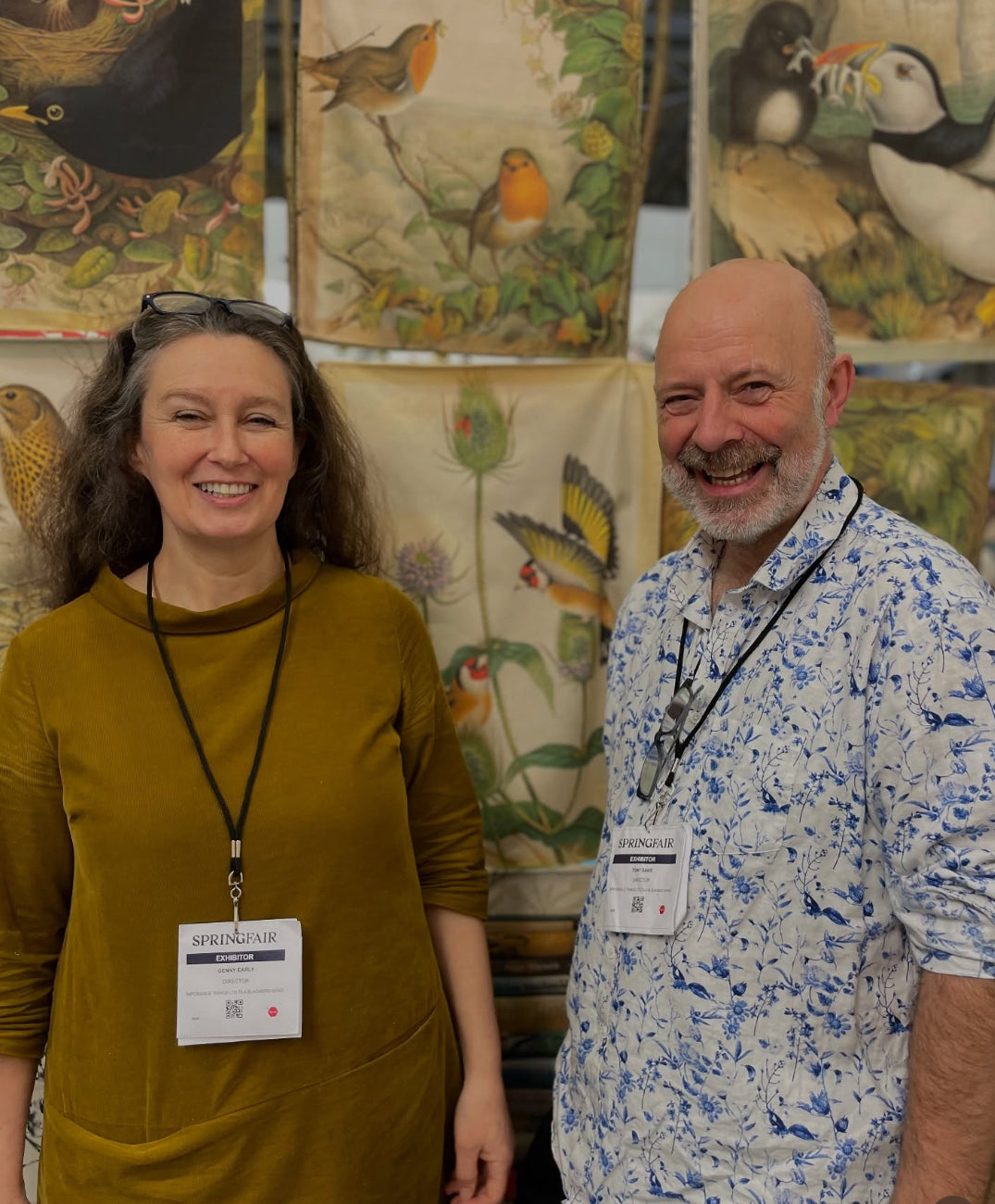 Two people standing in front of a display of fabric with bird designs.