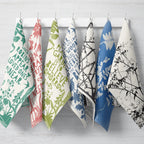 Set of colorful tea towels with various patterns hanging on a rack.
