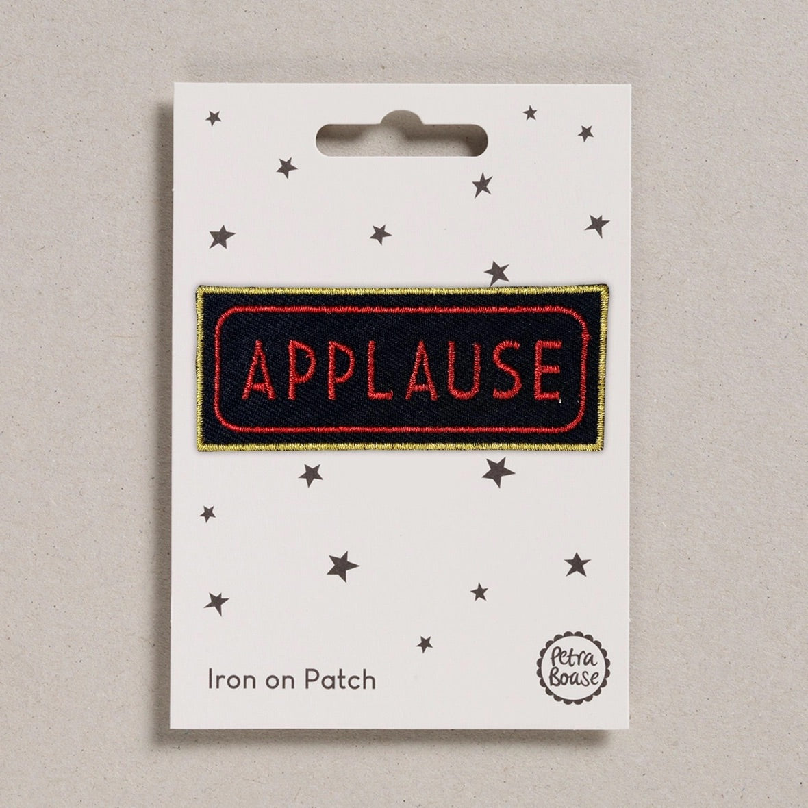 A rectangular iron-on patch with the word 'APPLAUSE' in red letters on a black background, outlined in gold, mounted on a white backing card decorated with small black stars and the text 'Iron on Patch' and 'Petra Boas'.
