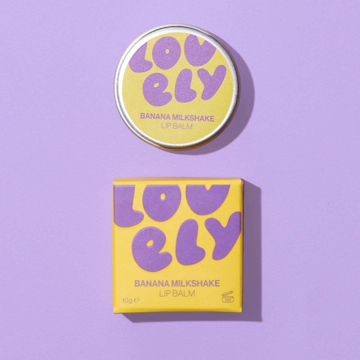 Banana Milkshake lip balm shown with its round tin lid and matching square box. The packaging features a bright yellow base with retro purple bubble lettering spelling 'LOVELY' and purple text identifying the flavor and product type.