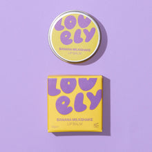 Banana Milkshake lip balm shown with its round tin lid and matching square box. The packaging features a bright yellow base with retro purple bubble lettering spelling 'LOVELY' and purple text identifying the flavor and product type.