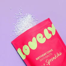 A pouch of bath salts, shown on a lavender background with white bath salts spilled from the top. The text reads 'BIRTHDAY CAKE BATH SALTS' and 'Jam + Sprinkles'.