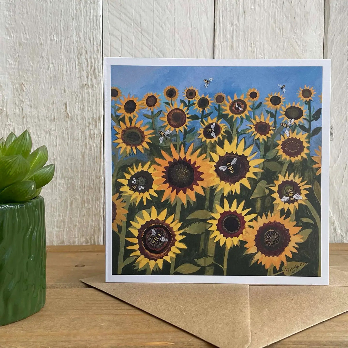 Greeting card with sunflower design on a wooden surface with a plant.