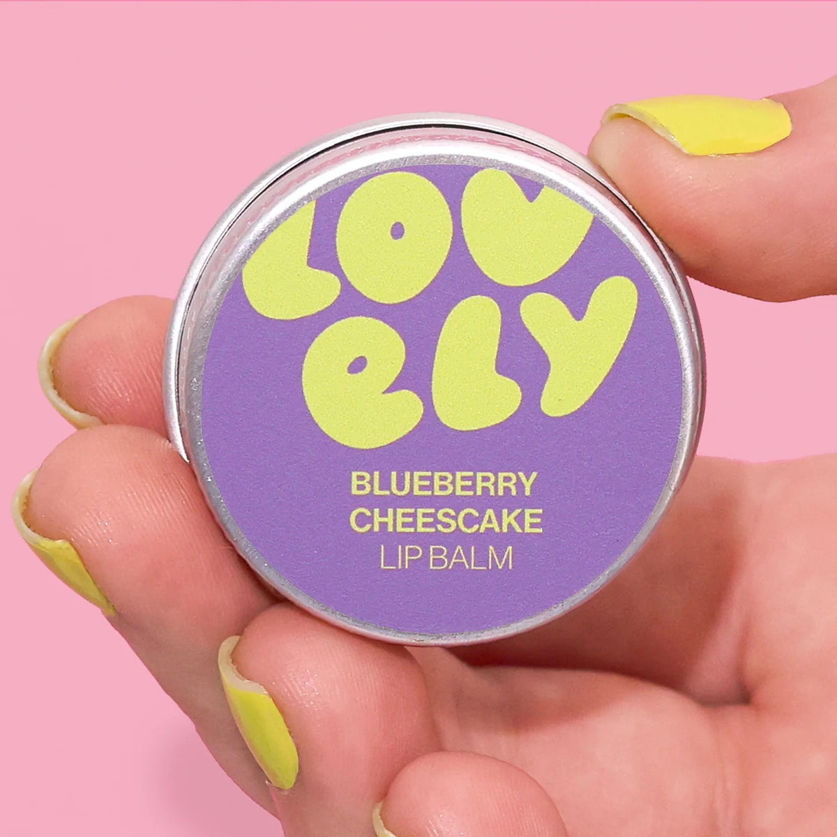 Lip balm container labeled 'Lovely' with 'Blueberry Cheesecake' flavor on a pink background.