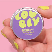Lip balm container labeled 'Lovely' with 'Blueberry Cheesecake' flavor on a pink background.