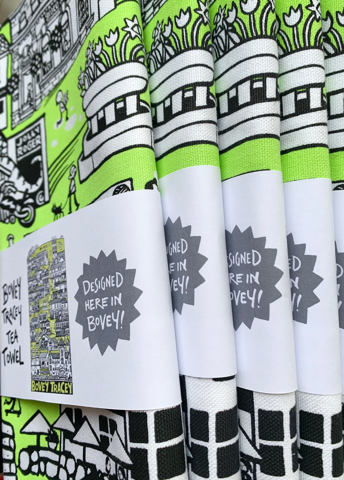 Tea towels with green, black, and white designs and paper sleeve with 'Designed here in Bovey' text.