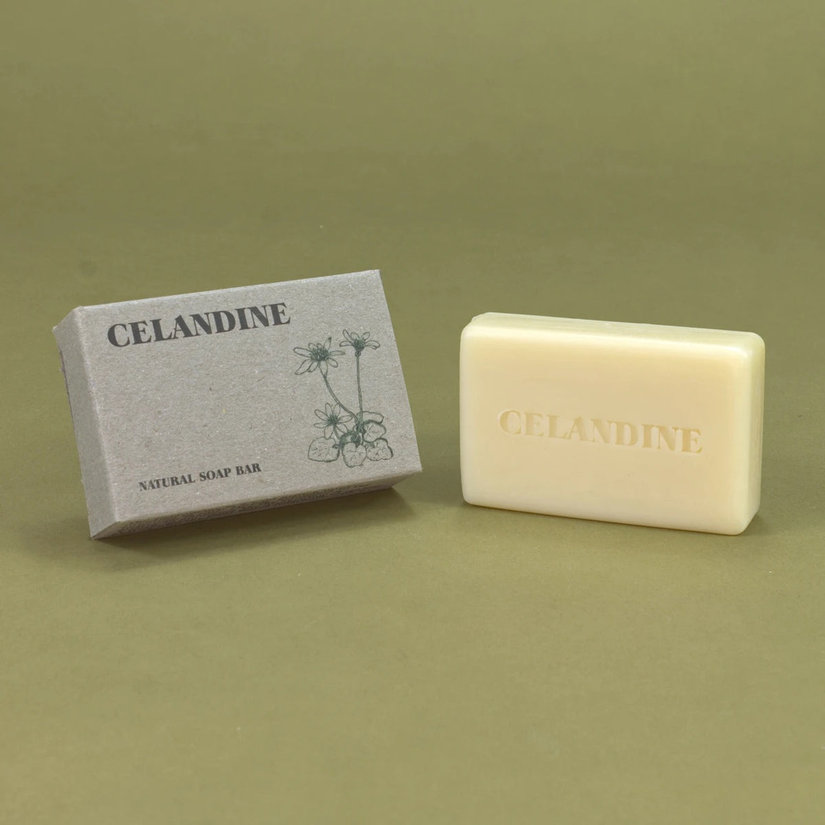 A cream-colored natural soap bar embossed with 'CELANDINE' sits next to its textured gray packaging box, both featuring the brand name 'CELANDINE' and a simple floral illustration, set against a solid olive green background.