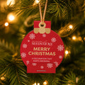 A red Seedsticks Christmas bauble hanging from a tree branch with warm string lights in the background. The lettering on the baubles reads 'MERRY CHRISTMAS' and 'A DECORATION THAT KEEPS GROWING'.