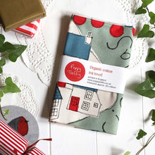 Organic cotton tea towel with festive village print in green, blue and red. Packaged with belly band