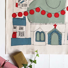 Close up of Organic cotton tea towel with festive village print in green, blue and red.