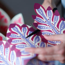 Person cutting out a purple and pink floral paper crown by Cambridge Imprint with scissors.