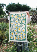 Daisy print tea towel on green background, displayed in a garden, held up by woman.