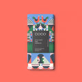 A dark chocolate bar with a colourful festive pattern and a dark central label reading 'COCO' and 'BLACK FOREST DARK CHOCOLATE', centered on a coral background.