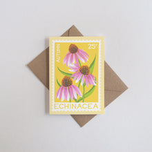 A rectangular greeting card featuring an illustration of three pink echinacea flowers with green stems on a yellow background. The card is placed on top of a brown envelope against a light gray background.