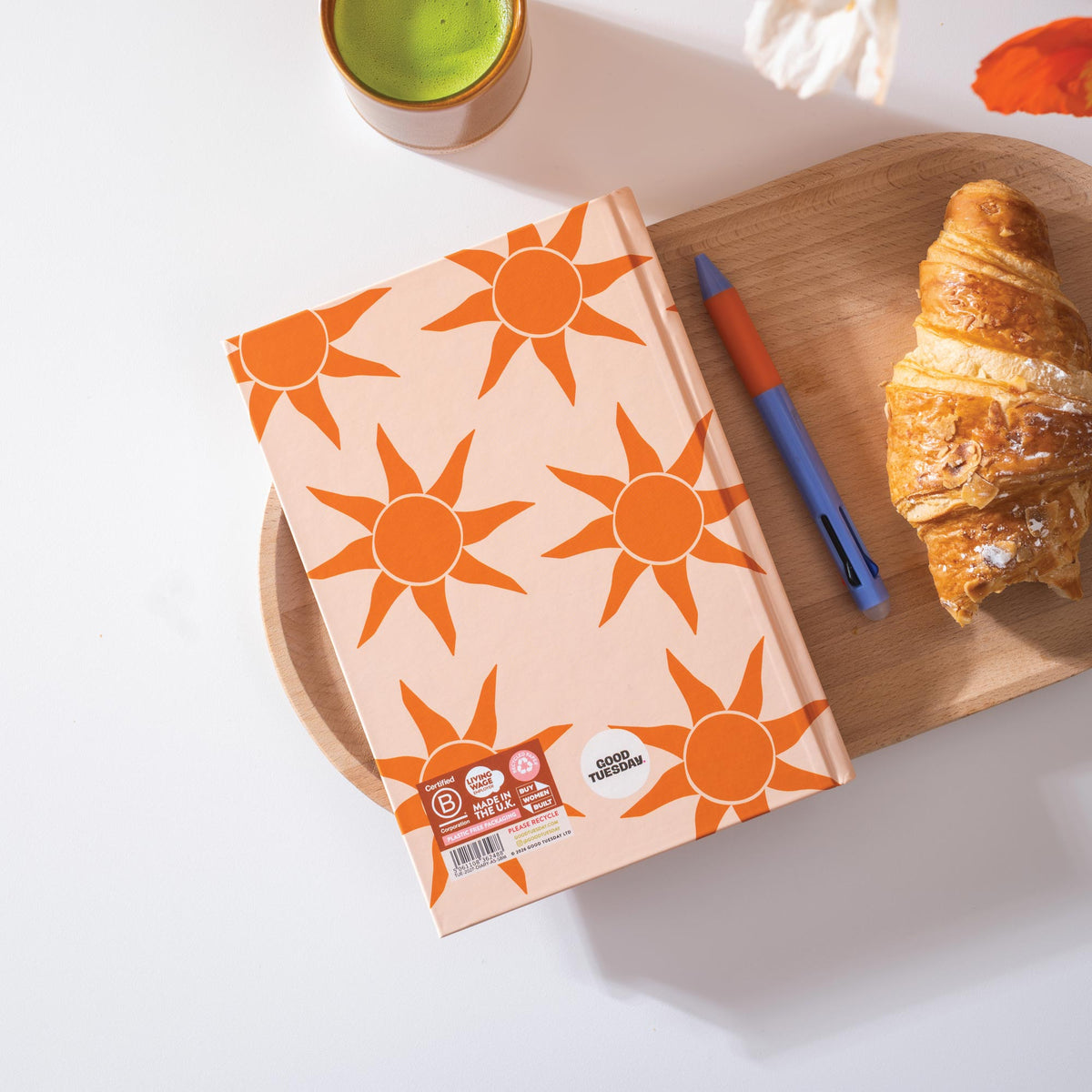 Reverse of diary with sun pattern, croissant, and pen on a wooden tray