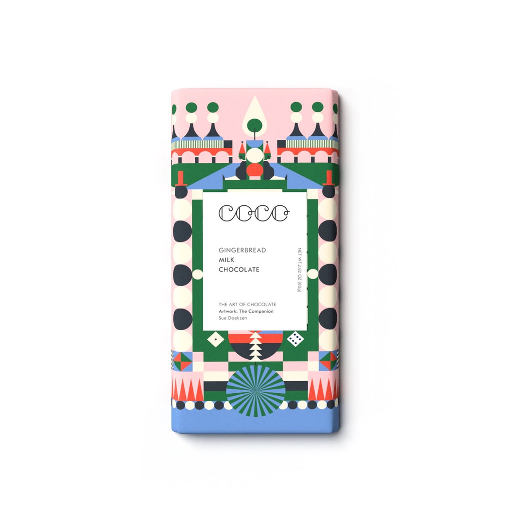 A single rectangular chocolate bar wrapped in a colorful geometric paper sleeve, centered on a plain white background. The wrapper features a pink top section, a blue bottom section, and a central white panel with black text reading 'COCO GINGERBREAD MILK CHOCOLATE'.