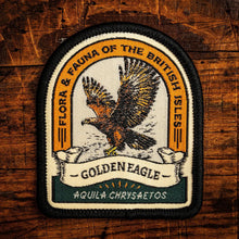 A rectangular embroidered patch with a black border and a central eagle design, reading 'FLORA & FAUNA OF THE BRITISH ISLES' and 'GOLDEN EAGLE', placed on a rustic wooden surface.