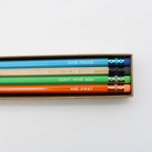 Four wooden pencils in blue, natural wood, green, and orange,  in a brown cardboard box. Each pencil features a humorous fishing-themed phrase from the TV show 'Gone Fishing'.