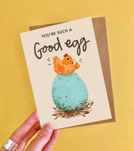 Card with a chicken on an egg and text 'You're such a good egg' held against a yellow background