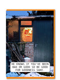  A Christmas card showing a snowy outdoor scene at dusk: a dark green garden shed door, brick wall, window with warm light, and a Santa face visible in the snow. A white speech-bubble text box at the bottom reads, 'HE KNOWS IF YOU'VE BEEN BAD OR GOOD SO BE GOOD FOR GOODNESS SAKE. 