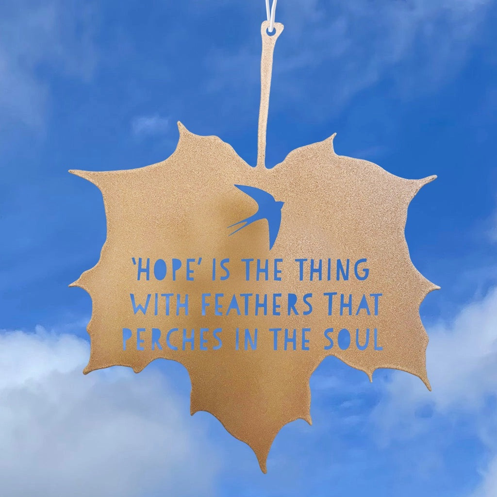 Decorative leaf-shaped sign with a bird and inspirational quote against a blue sky.
