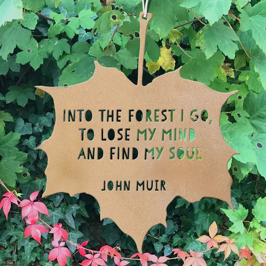 Leaf-shaped sign with John Muir quote on a green leafy background