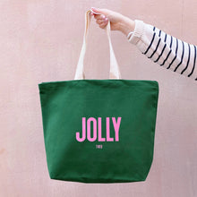Green tote bag with 'JOLLY TIRED' text held by a person against a pink background