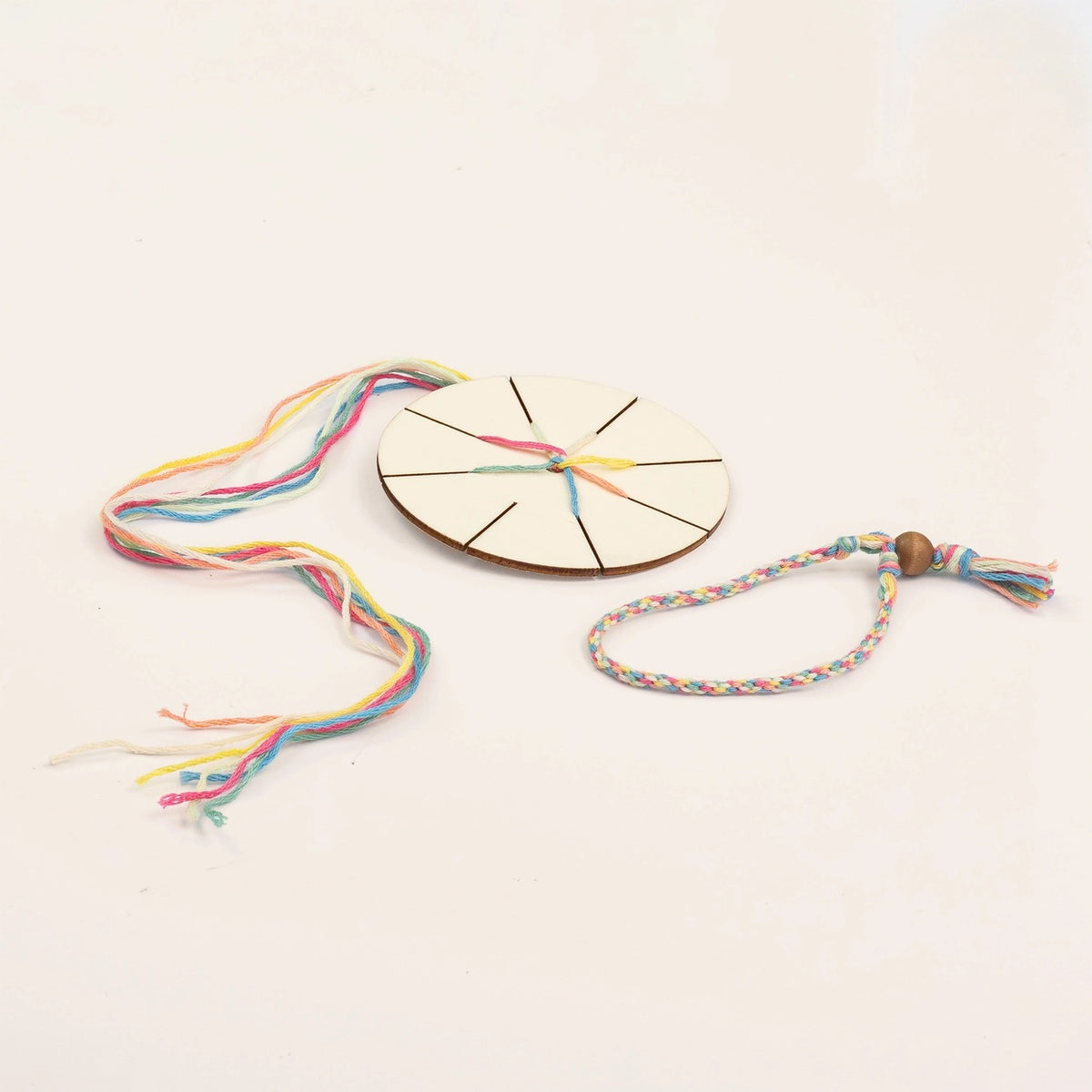 Colourful friendship bracelet-making kit with a wooden disc and threads on a light background