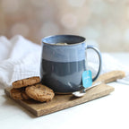 Blue mug with a tea bag on a wooden tray with cookies and a spoon.