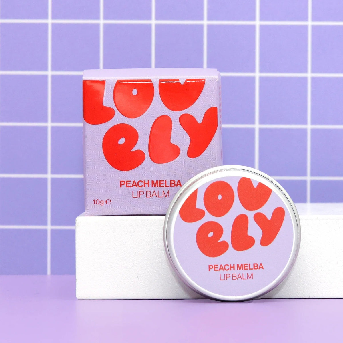 Lovely Skincare's Peach Melba lip balm with packaging on a purple grid background