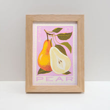 A framed art print featuring an illustration of a pear and a cut pear on a pink background, displayed in a light oak wood frame against a neutral gray background.
