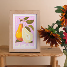 A framed art print featuring an autumn pear illustration in a light wood frame, styled on a wooden table next to sunflowers against a beige wall.