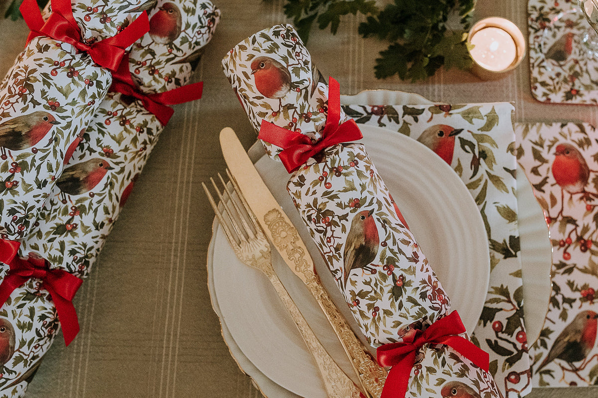 A Christmas table featuring Robin print Christmas crackers and matching napkins with candles and foliage.
