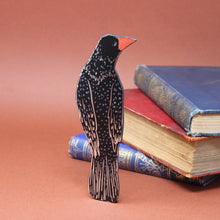 Black and silver rook bookmark made from leather with silver foil details, standing against a background of vintage books.  