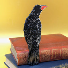 Black rook leather bookmark on top of a stack of books with a yellow background