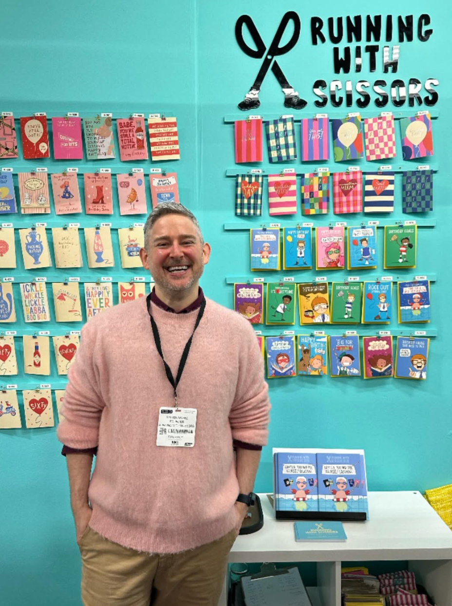 Steven from Running with Scissors in front of a wall with greetings cards.