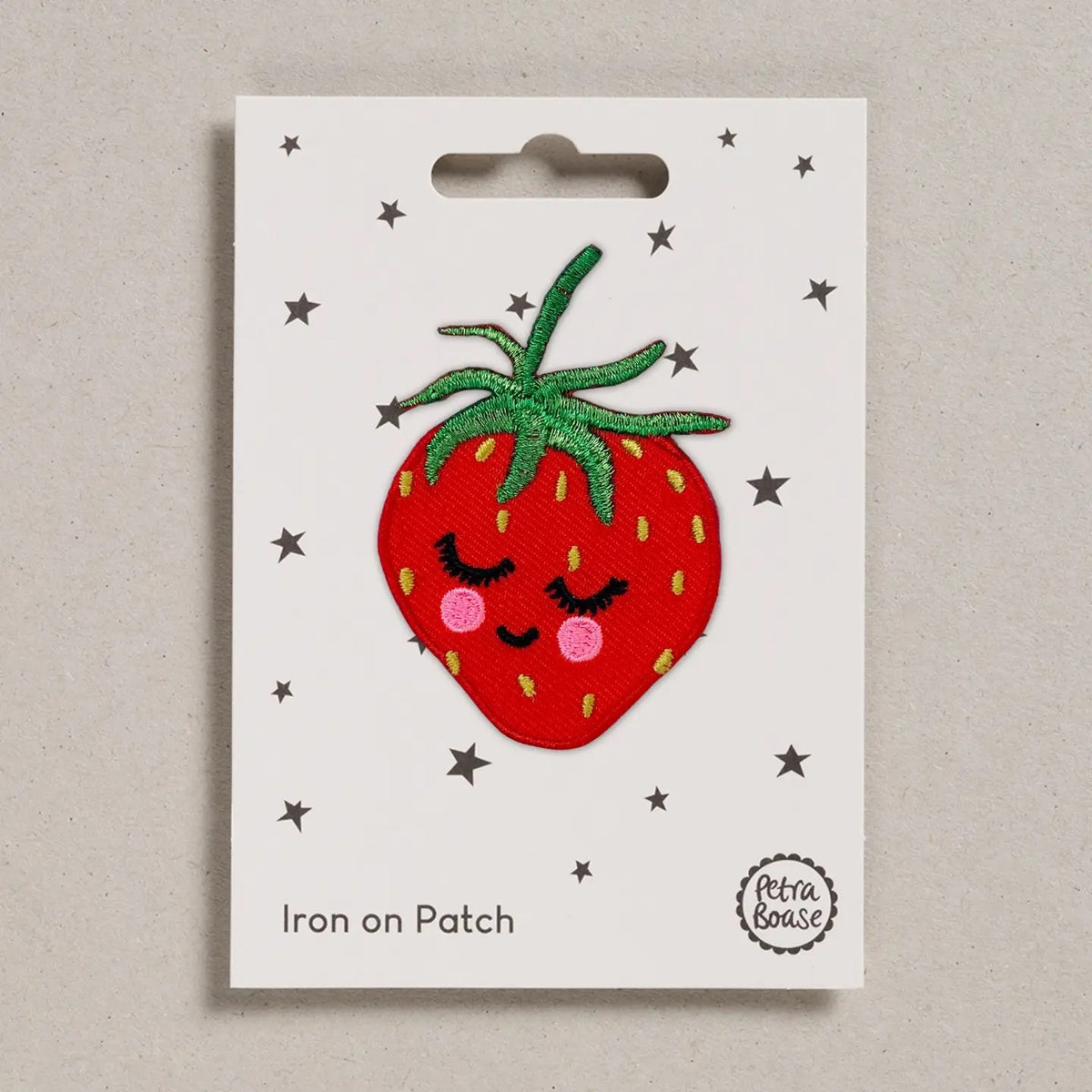 A strawberry-shaped iron-on patch with a sleeping face, displayed on its white backing card. The backing card features small silver stars, the text 'Iron on Patch' at the bottom left, and a circular logo for 'Petra Boase' at the bottom right.