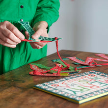 Person in a green shirt threading letters onto Merry Christmas banner by Cambridge Imprint