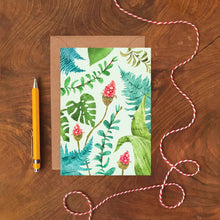 Greeting card with tropical leaves and floral design on a wooden surface with a pen and string.