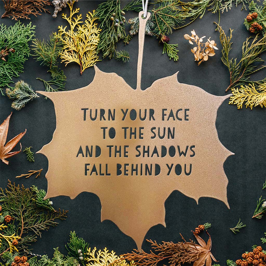 Decorative leaf-shaped sign with motivational quote surrounded by natural elements on a dark background