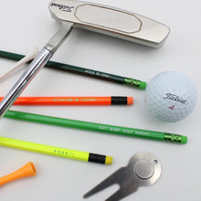 Four pencils with golfing terms are displayed with a set of golf accessories arranged on a white background, including a silver putter, a white Titleist golf ball,.