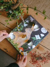 Advent calendar with hare design and open doors showing individual tea light candles. Shown on a wooden table with greenery surrounding.
