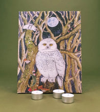 Advent Calendar featuring a snowy owl perched among bare tree branches under a full moon, displayed on an olive green surface with three silver tea light candles in front.