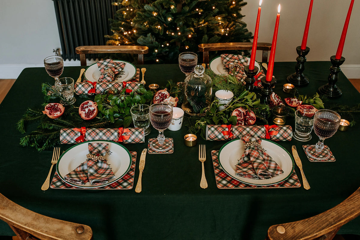 Christmas table set with tartan crackers and napkins and red dinner candles with green foliage.